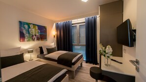 A modern hotel room with two beds, a desk, a TV, and a painting on the wall. - Design apartment for 3-5 people with south-facing loggia and garden view. Near the lake! (Bensheim)
