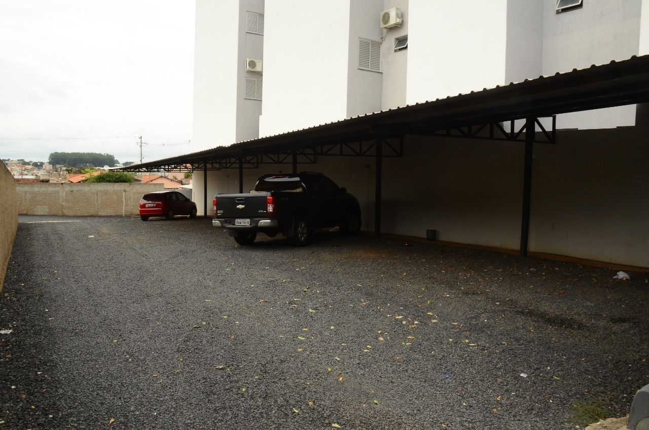 Un área de estacionamiento techada con dos vehículos: un coche rojo y una camioneta SUV negra, estacionados bajo una estructura de techo metálico.