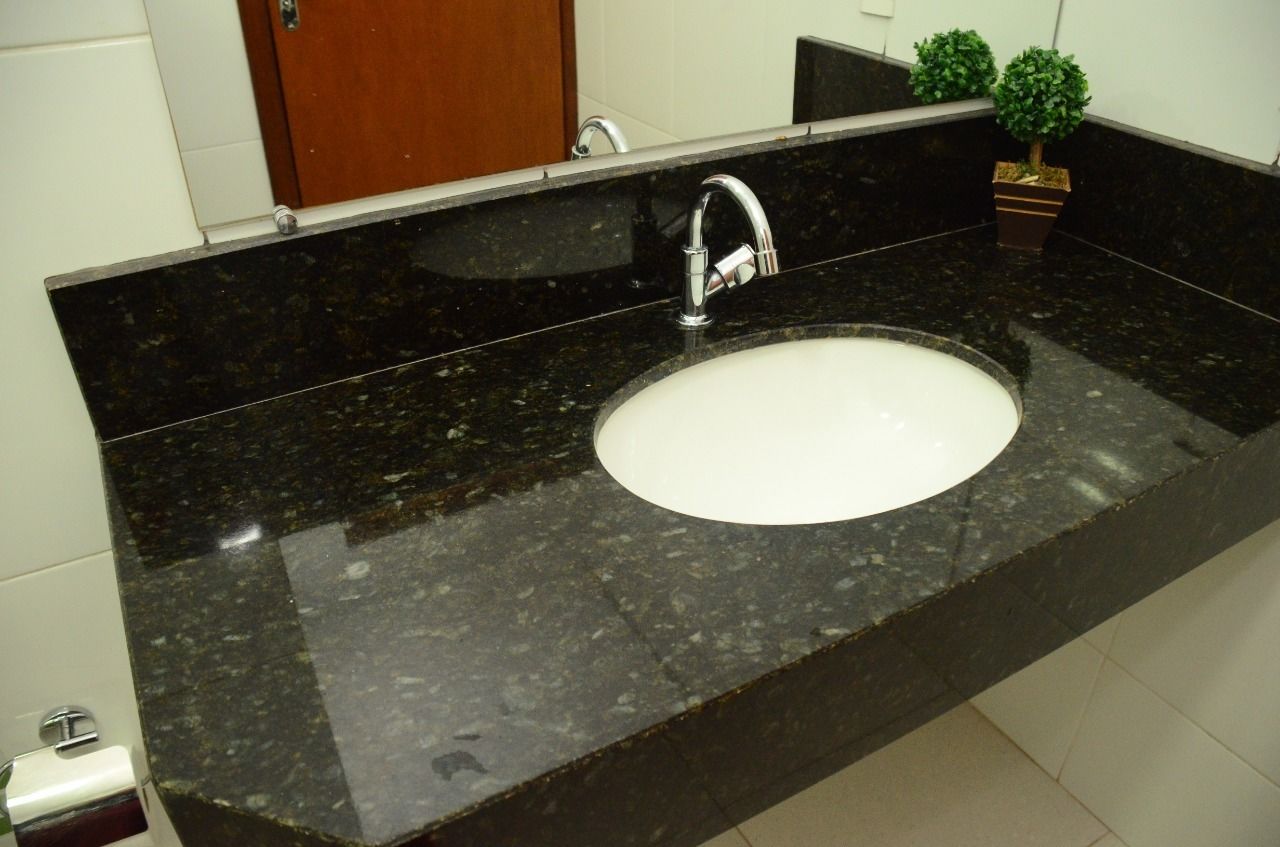 A bathroom with a black granite countertop, a white sink, and a small potted plant.