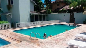 Ein rechteckiger Pool mit einer gefliesten Liegefläche, einem weißen Zaun und einigen darin schwimmenden Personen.