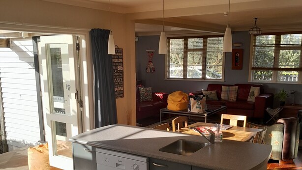 Een moderne keuken met een ingebouwde vaatwasser, een groot eiland met een spoelbak en een eetgedeelte met een rode bank en een houten tafel.
