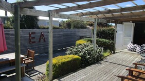 Een houten terras met een pergola, een bankje en een muur met de letters 'EA'.