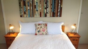 Een opgemaakt bed met witte lakens, een bloemenkussen en twee bedlampen op houten nachtkastjes.