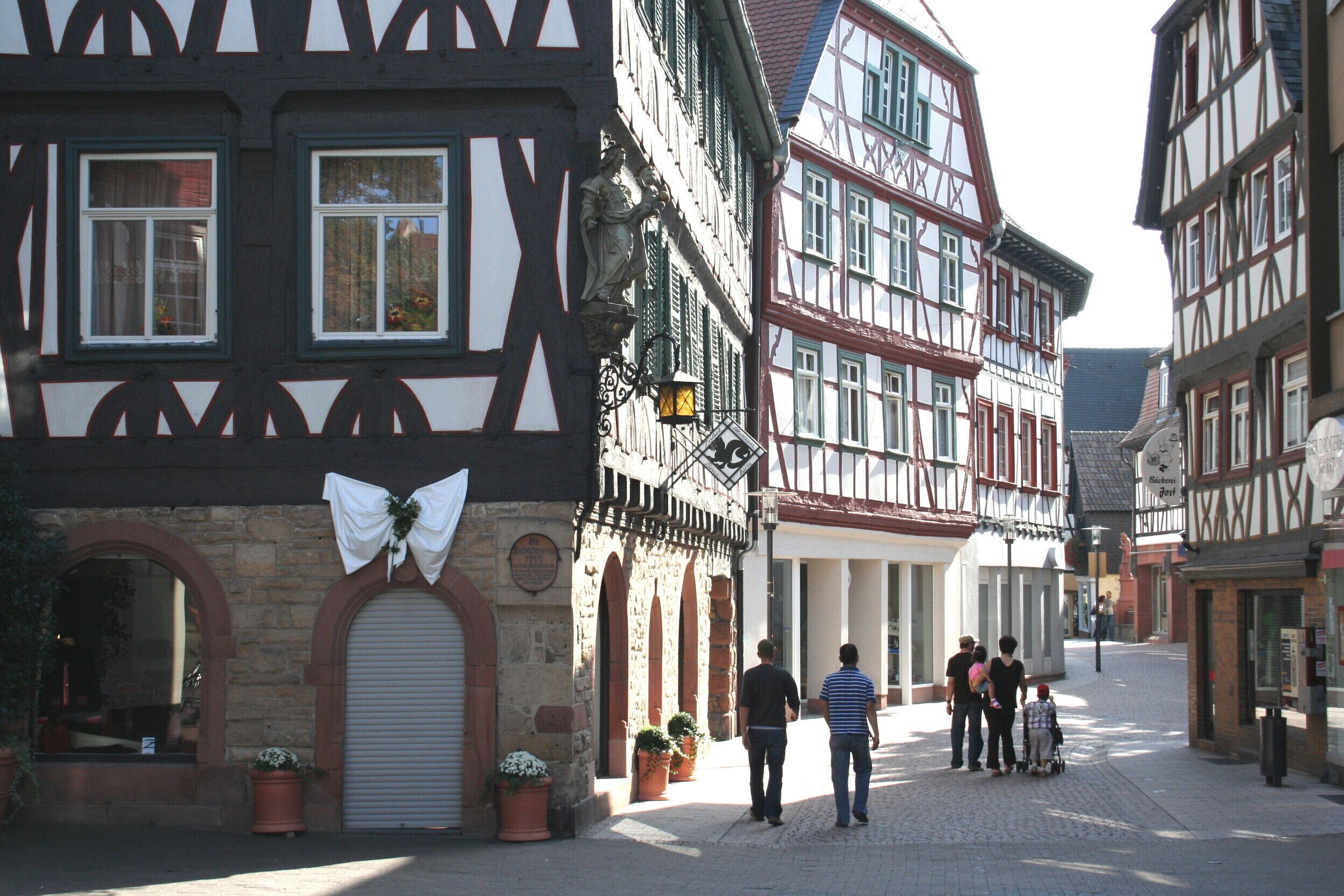 Eine typische europäische Straße mit Fachwerkhäusern, ein Geschäft mit weißem Markisenbändchen und eine Gruppe von Menschen, die unterwegs sind.