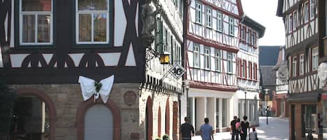 A traditional European street with half-timbered buildings, a closed shop with a white awning, and a group of people walking.