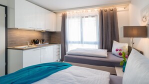 A modern hotel room with a kitchenette, a bed with a teal throw, and a window with curtains. - "Bathroom apartment" for bathing beauties with Roman bath tub / 1-2P / Parking free! (Bensheim)