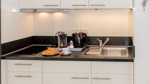 A modern kitchen with white cabinets, a black countertop, a coffee maker, and a sink. - "Bathroom apartment" for bathing beauties with Roman bath tub / 1-2P / Parking free! (Bensheim)