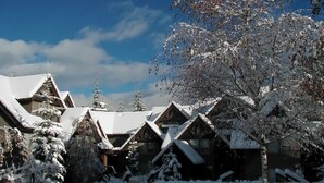 Un chalet enneigé comprenant plusieurs cabanes, chacune dotée d’un toit en pente et entourée d’arbres chargés de neige.