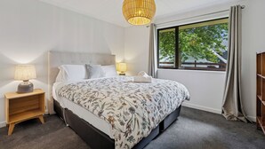 A neatly arranged bedroom with a large bed, bedside lamps, a window with a view, and a hanging light fixture. - Rees on Reid - Arrowtown Holiday Home (Arrowtown)