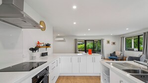 A modern kitchen with white cabinetry, a black stovetop, and a wooden floor. - Rees on Reid - Arrowtown Holiday Home (Arrowtown)