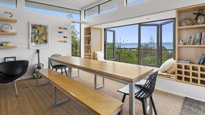 Ein moderner Essbereich mit Holztisch und Bänken, einer Gitarre und Blick auf das Meer durch große Fenster.