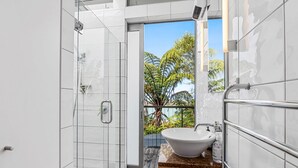 Ein modernes Badezimmer mit einer gläsernen Duschkabine, einem freistehenden Waschbecken und Blick auf üppige tropische Pflanzen.
