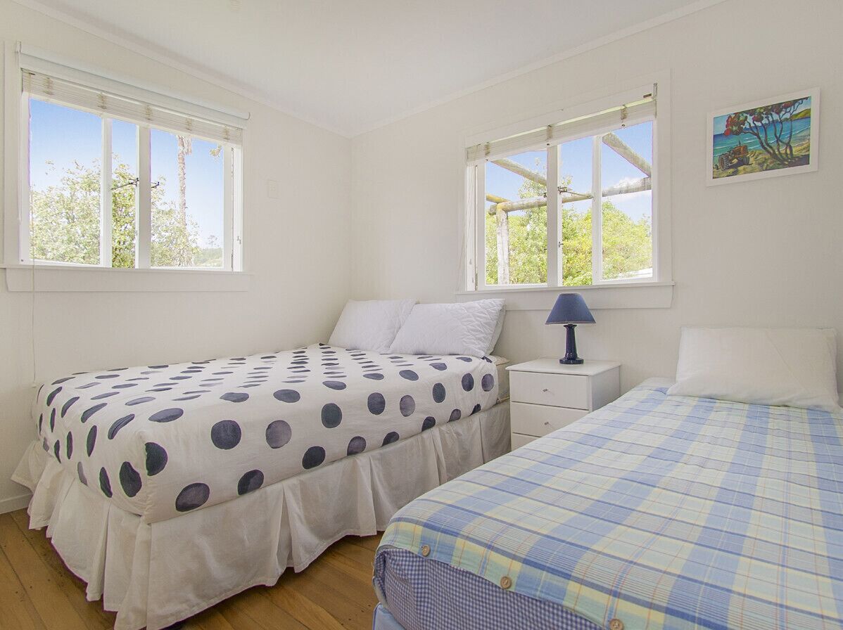 Une chambre avec deux lits, chacun recouvert d’une couvre-lit à motifs différents, une table de chevet avec une lampe et une fenêtre donnant sur des arbres.