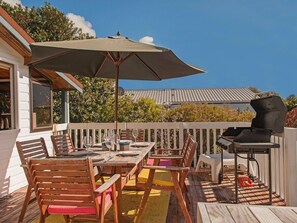 Eine Terrrasse im Freien mit Holztisch und -stühlen, einem Grill und einem großen Sonnenschirm.