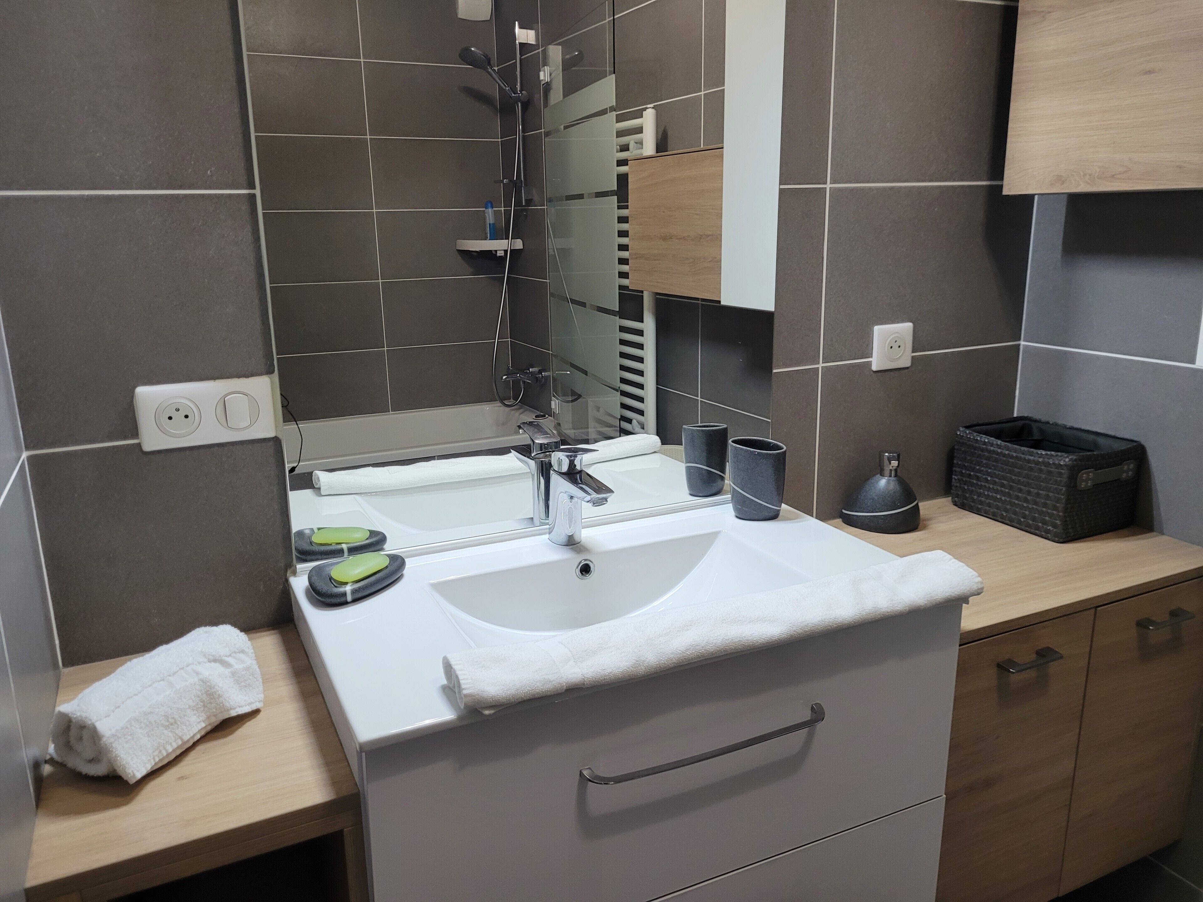 Une salle de bain moderne avec un lavabo blanc, un miroir et deux tasses noires posées sur le comptoir.