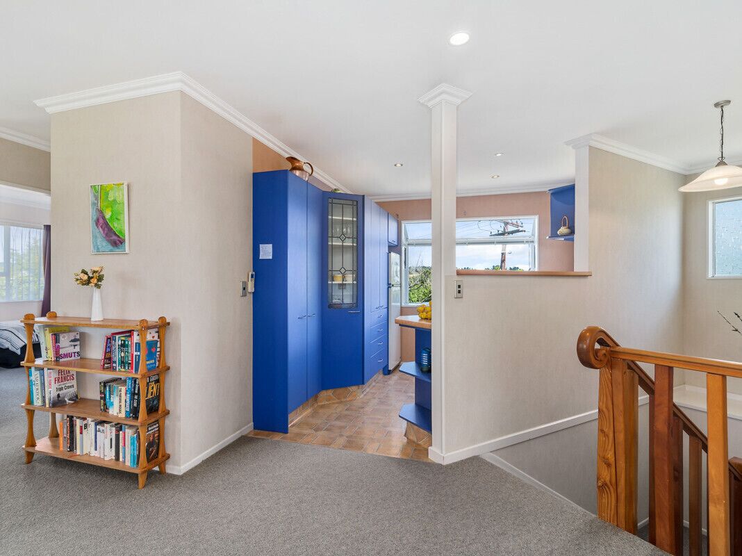 A hallway with a blue door, a bookshelf, and a staircase.