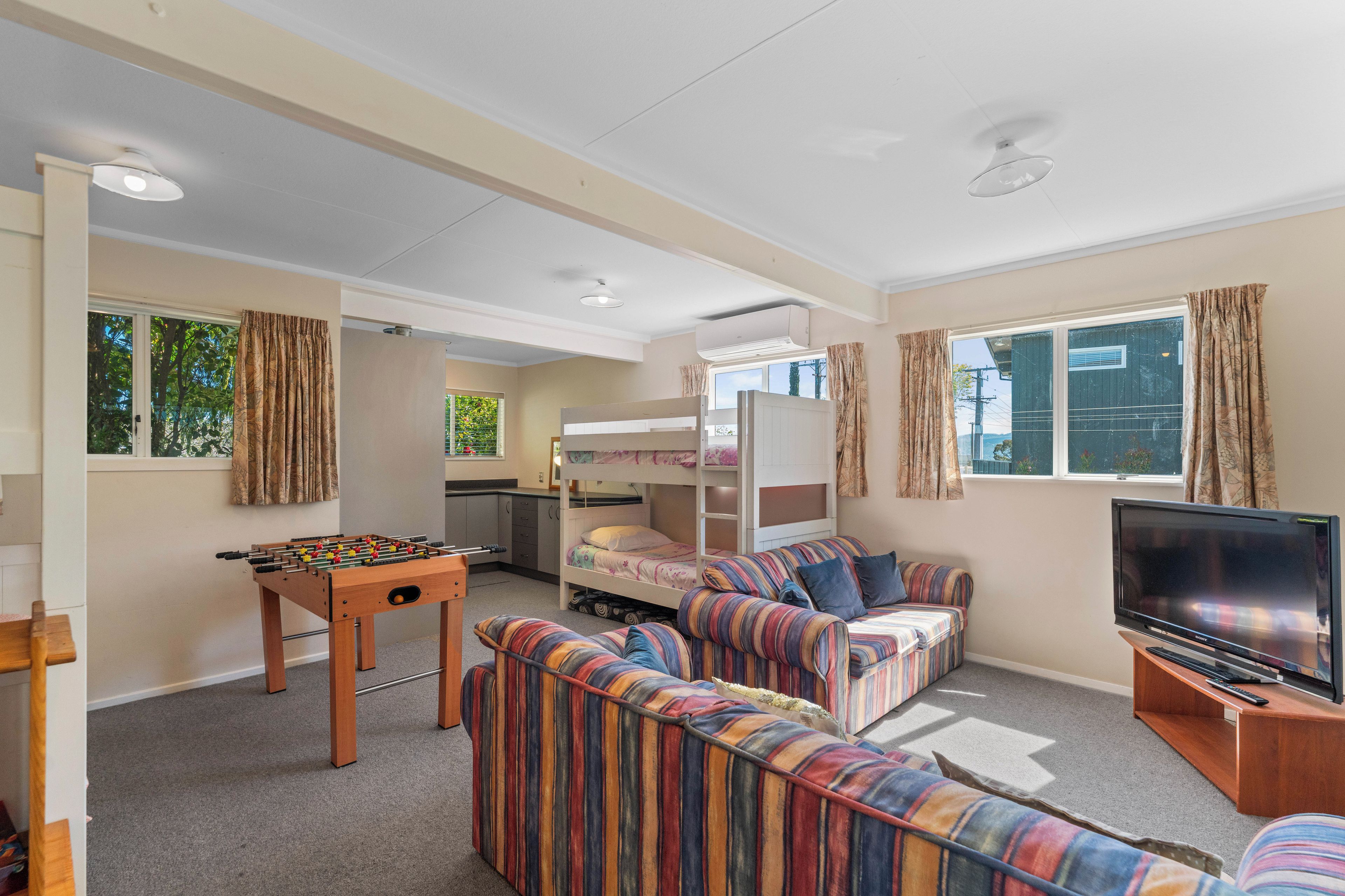A furnished room with a sofa, a foosball table, a bunk bed, a television, and a window with curtains.