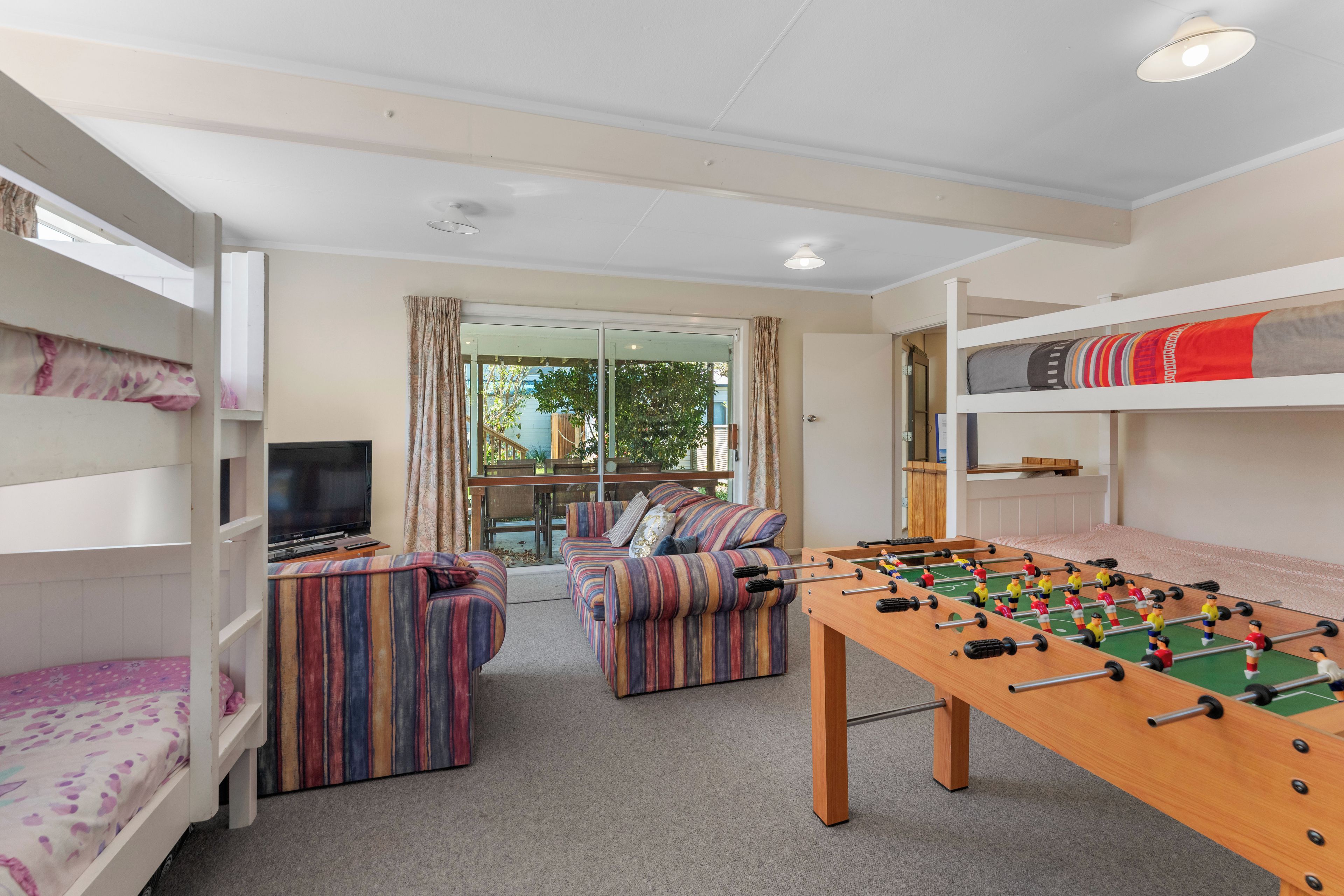 A room with bunk beds, a sofa set, a foosball table, and a television.