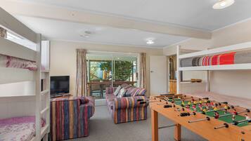 A room with bunk beds, a sofa set, a foosball table, and a television.