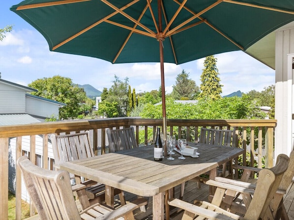 A wooden deck with a table and chairs, an umbrella, and a bottle of wine.