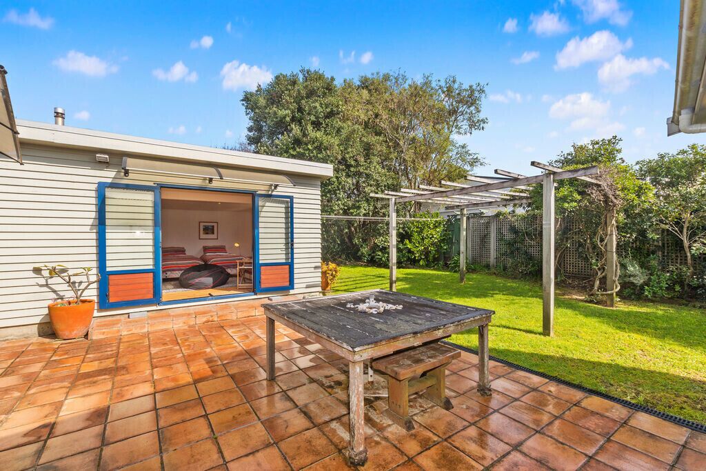 Um pátio com mesa e cadeiras de madeira, área de estar coberta e uma casa com porta de garagem.
