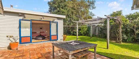 Um pátio com mesa e cadeiras de madeira, área de estar coberta e uma casa com porta de garagem.
