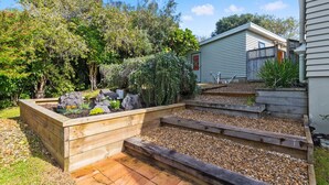 A garden with raised beds, a wooden deck, and a small shed. - Taste Of Paradise with WiFi!- Mangawhai Heads Home (Mangawhai Heads)