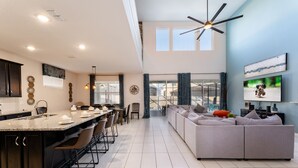 Una cocina moderna con una isla grande, comedor y sala de estar con sofá y televisor.