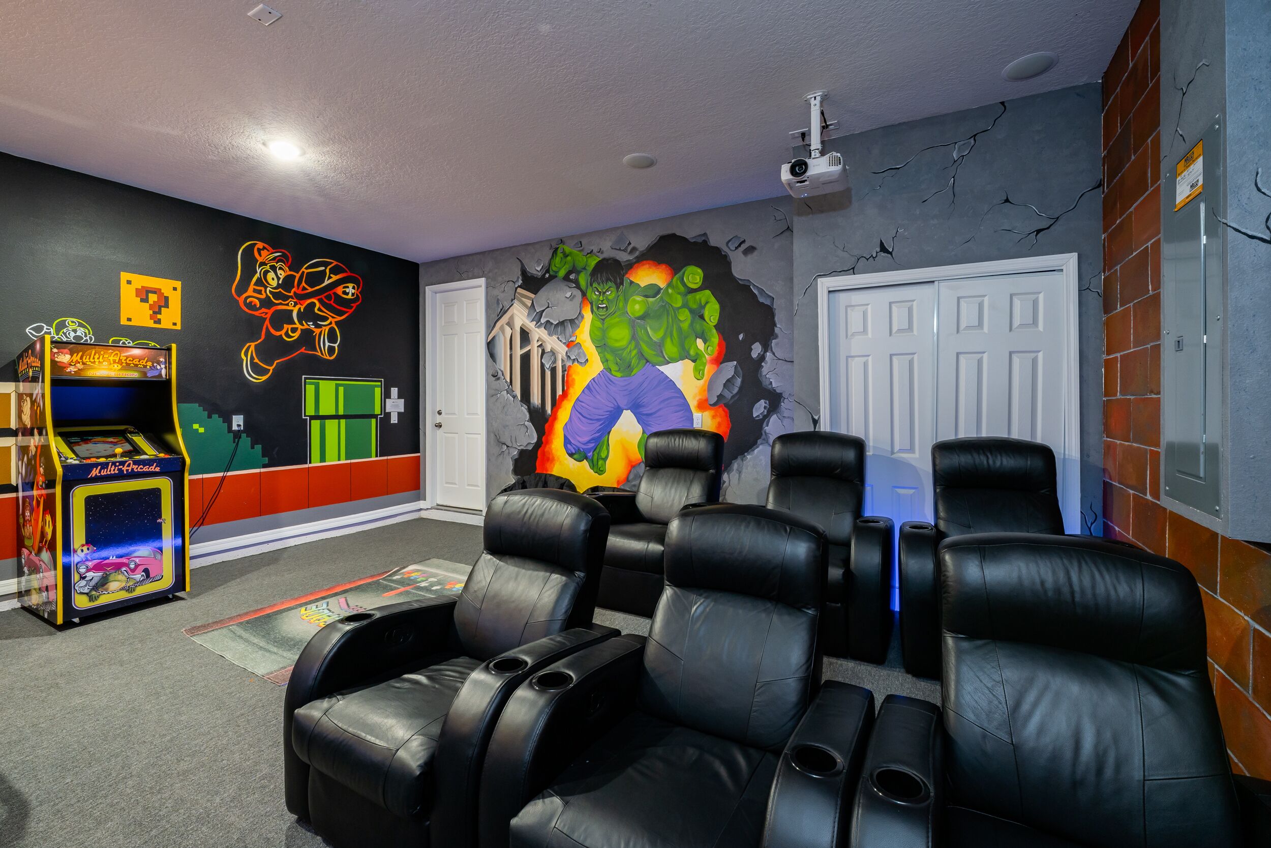 Une pièce comprenant une salle d’arcade, une fresque représentant un personnage vert et des fauteuils en cuir noir.