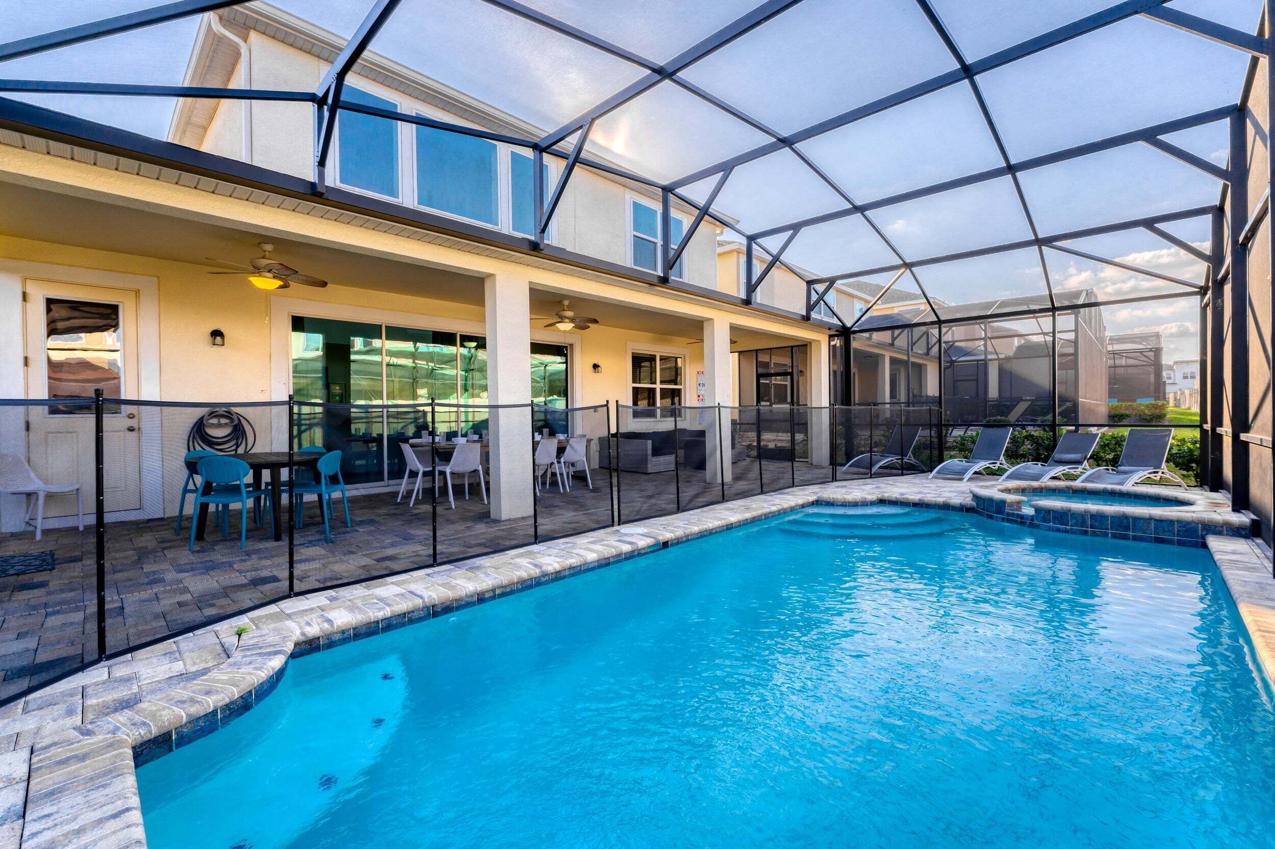 A swimming pool with a glass-enclosed patio area, outdoor seating, and a view of neighboring houses.