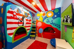 Una sala de juegos infantil con murales coloridos, un tobogán y una escalera.