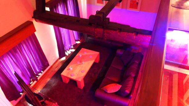 A room with a wooden ceiling structure, a sofa, a small table, and a window with curtains. - Loft in Red Light District (Antwerpen)