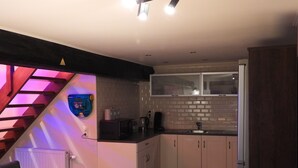 A compact kitchen with a brick backsplash, wooden cabinets, and a dining area with a table and chairs. - Loft in Red Light District (Antwerpen)