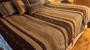 Het interieur van een houten hutje, met een groot bed, een gestreept dekbed en meerdere kussens.