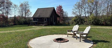 A wooden house with a fenced yard, two Adirondack chairs, and a fire pit.
