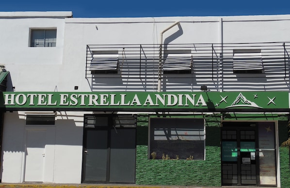 Un hotel llamado "HOTEL ESTRELLA ANDINA" con un toldo verde, un ventanal con vista a plantas y un cartel con el nombre del hotel.