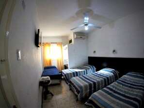 Habitación de hotel con dos camas individuales, un escritorio, una silla, un ventilador de techo y una ventana con cortinas.
