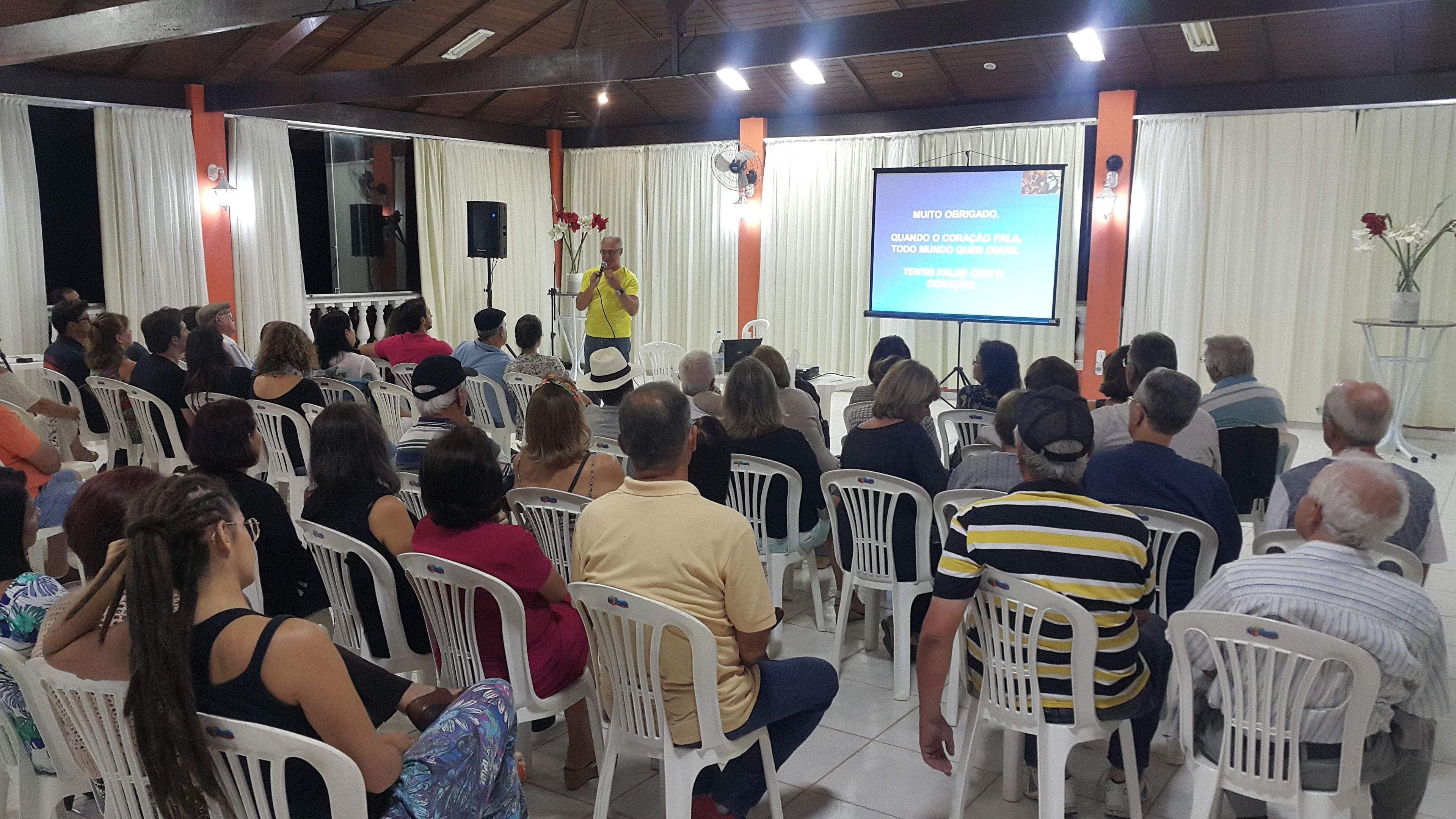 Un salón de conferencias con asistentes sentados en sillas blancas mirando a un orador en un atril.