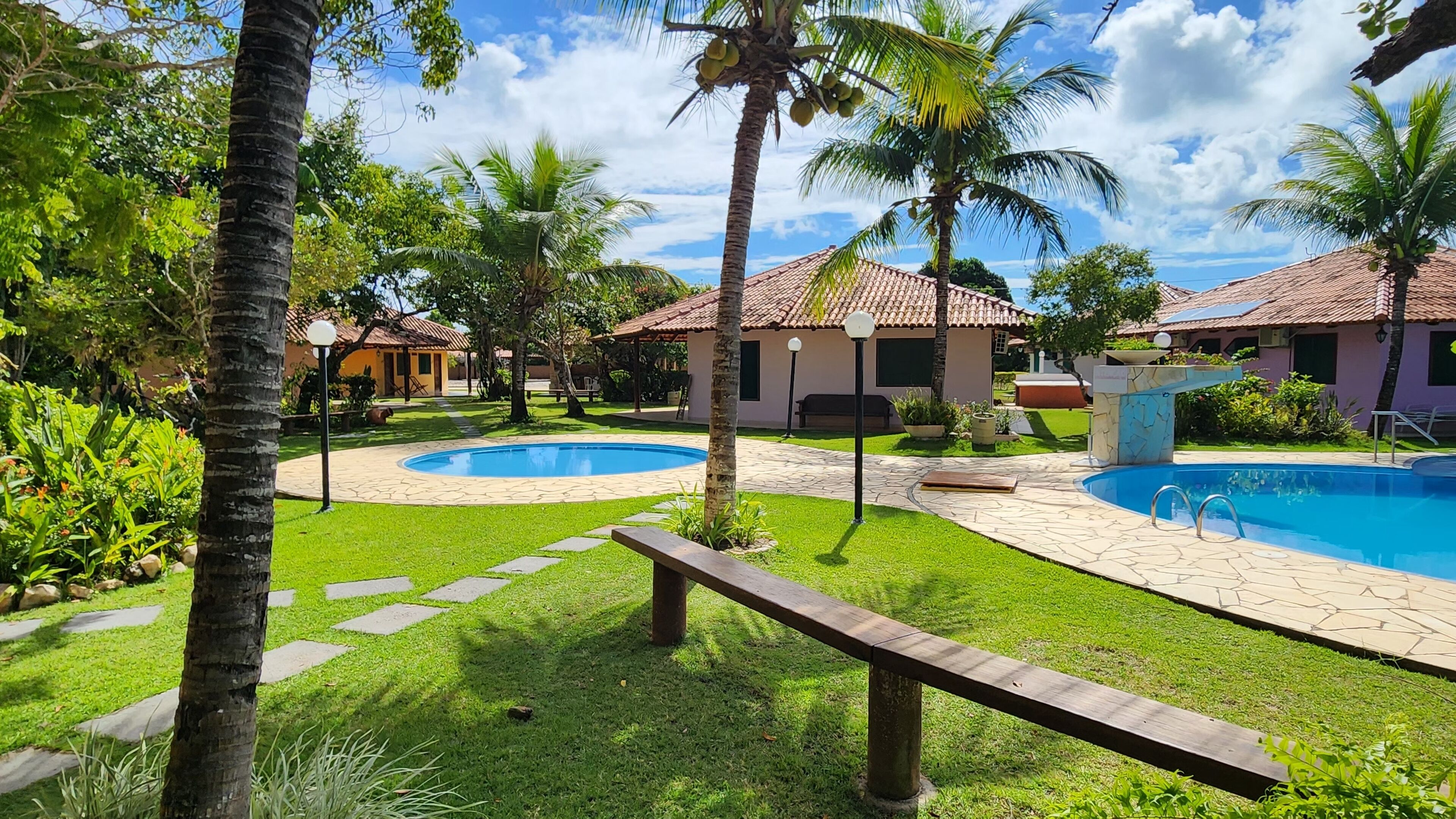 A resort with two swimming pools, palm trees, and a well-maintained lawn.