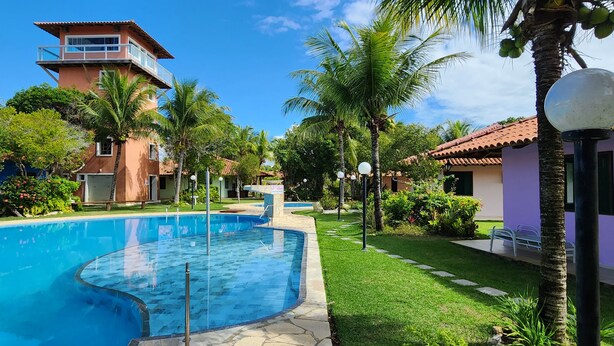 A swimming pool surrounded by lush greenery and a building with a red-tiled roof.