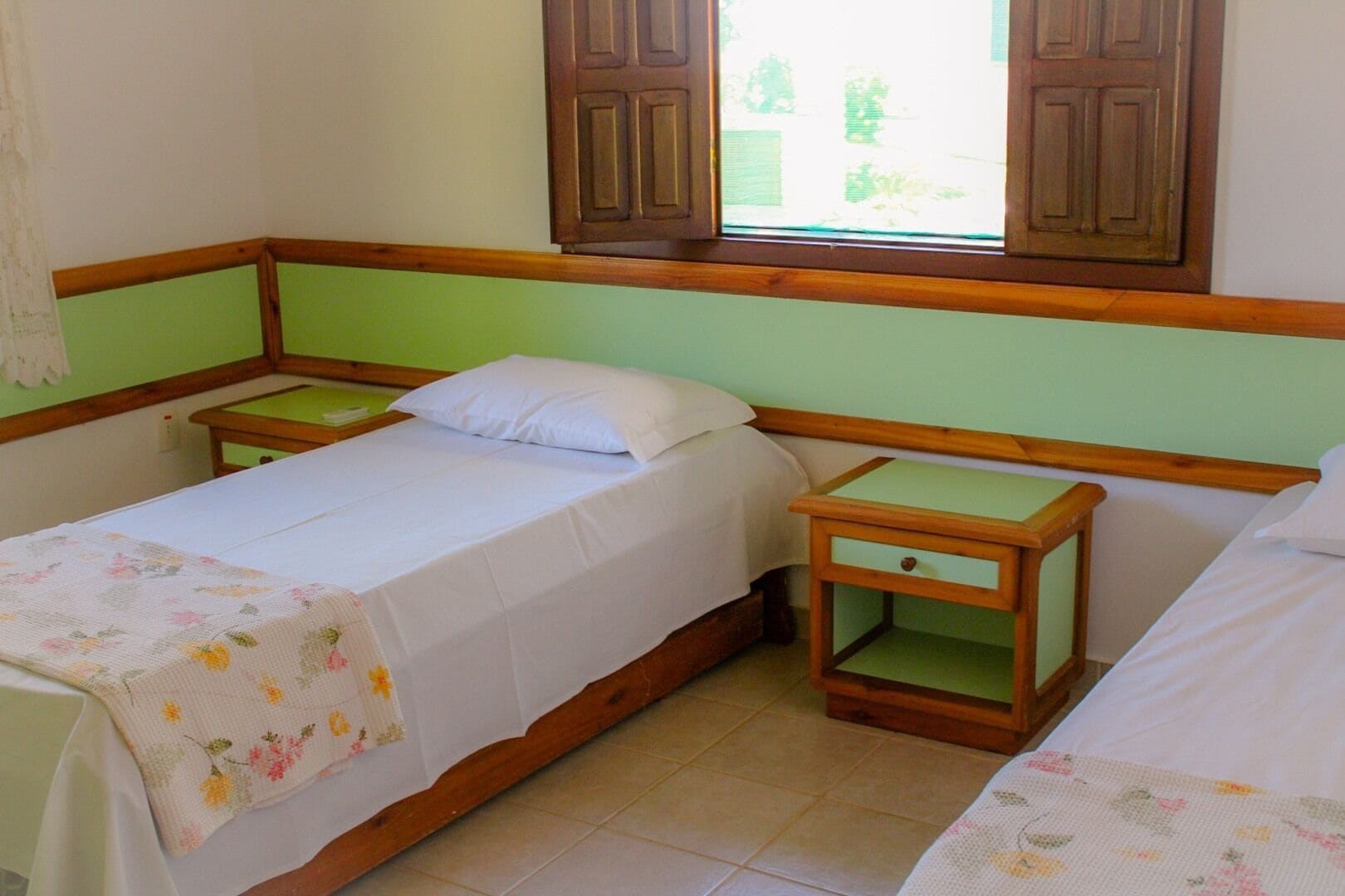 Une chambre avec deux lits simples, des tables de chevet en bois et une fenêtre avec des volets en bois.
