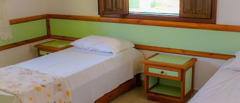 A room with two single beds, wooden nightstands, and a window with wooden shutters.