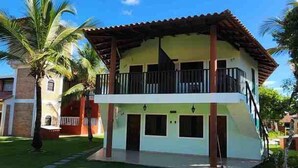 A two-story house with a balcony, surrounded by a well-maintained lawn and palm trees.