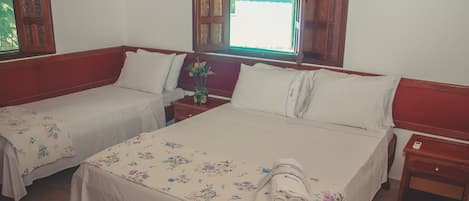 Habitación de hotel con dos camas individuales, cabecero de madera, mesita de noche con un jarrón de flores y ventana con vistas al exterior.
