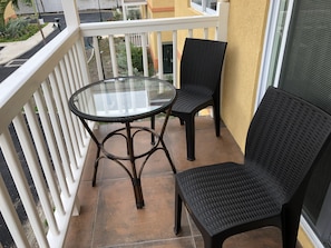 Enjoy a peaceful moment on this balcony with a glass-top table and two wicker chairs.