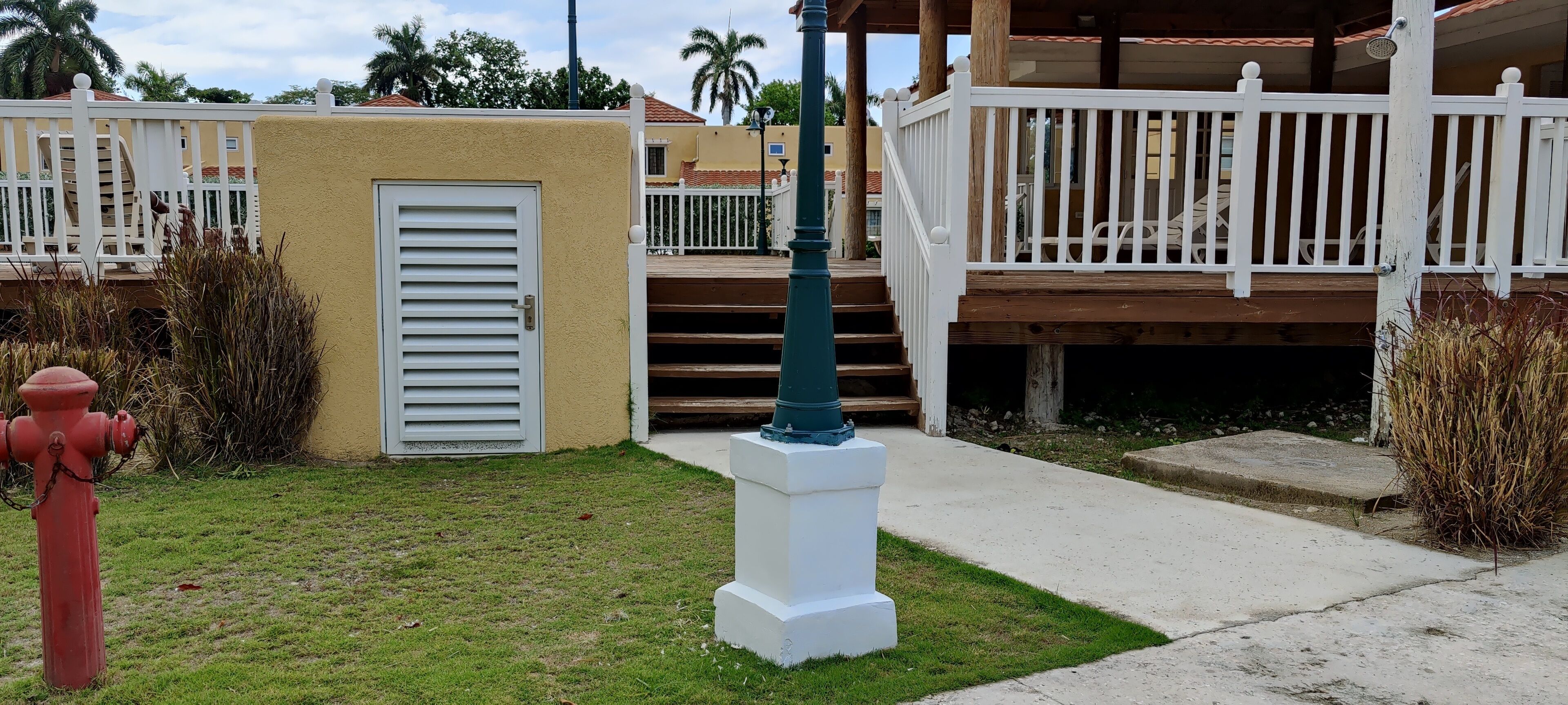Un quartiere residenziale con una porta bianca, un idrante rosso, una cassetta delle lettere bianca e una scala in legno che conduce a un balcone.