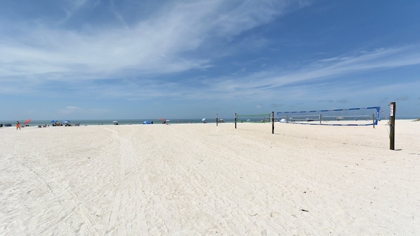A beach volleyball court with a net and posts, surrounded by sand.