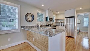 A modern kitchen with a granite countertop, stainless steel appliances, and a wooden floor. - Classic Folly Cottage (Folly Beach)