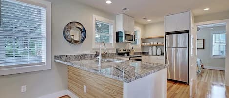 Una cocina moderna con encimera de granito, electrodomésticos de acero inoxidable y suelo de madera.