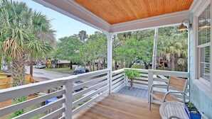 A covered porch with a wooden ceiling, white railings, and a bench. - Classic Folly Cottage (Folly Beach)